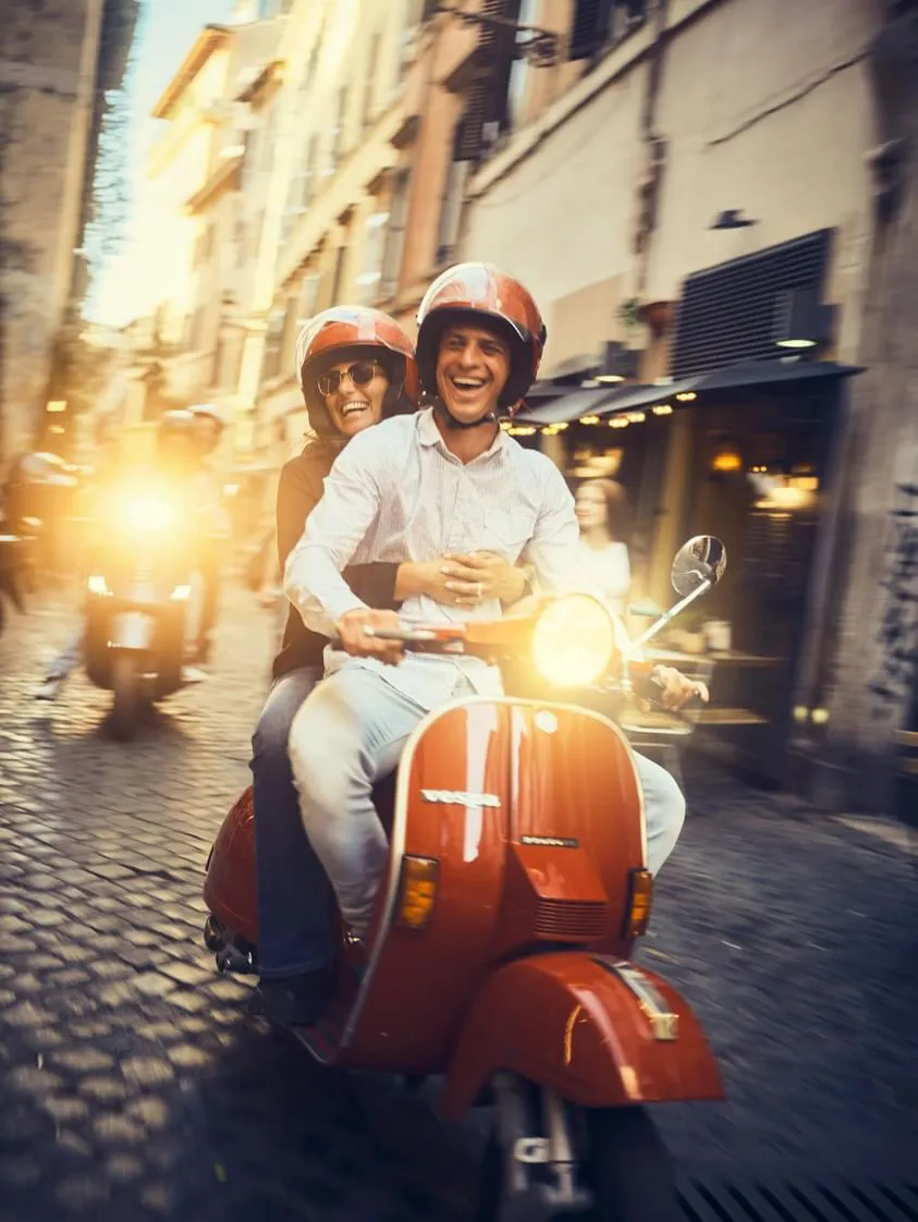 Couple on a Vespa through the lit alleys of the historic centre at sunset